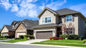Beautiful two-story siding home with brick trim, dark shutters, and a neat lawn under a blue sky with clouds.