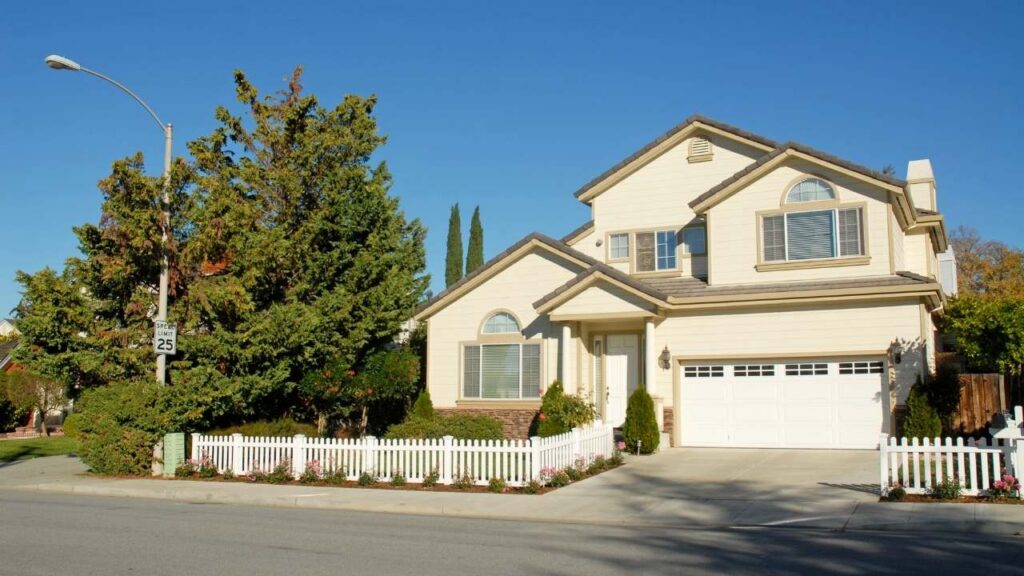 Cream-colored two-story suburban family home with a concrete driveway under a clear sky.