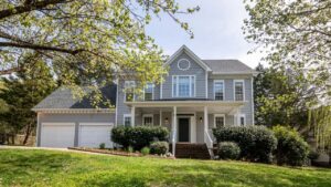 Stately two-story gray craftsman-style house with detailed white gables and a lush green front lawn.
