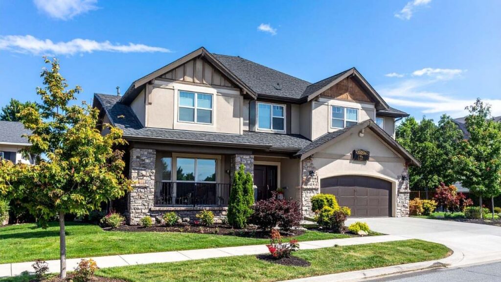Modern two-story dark grey siding home with large rectangular windows and a lush green front lawn.