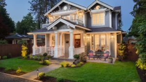 Elegant grey siding two-story house featuring a front porch with white columns and landscaped bushes.